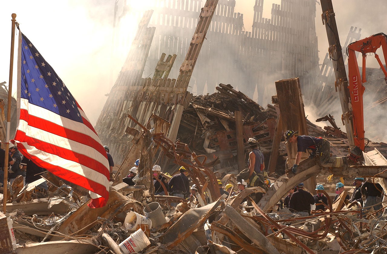 Rescue workers climb through rubble and smoke at the World Trade Center site, and an American flag flies at left